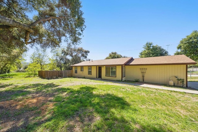 rear view of property featuring a lawn and fence
