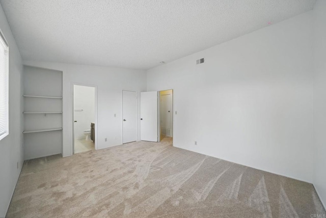 unfurnished bedroom with carpet flooring, a textured ceiling, visible vents, and ensuite bath