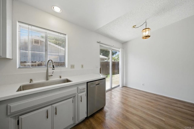 kitchen featuring stainless steel dishwasher, light countertops, a textured ceiling, a sink, and dark wood finished floors