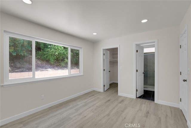 unfurnished bedroom featuring baseboards, wood finished floors, a spacious closet, and multiple windows