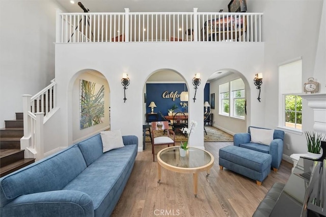 living room with stairs, arched walkways, a high ceiling, and wood finished floors