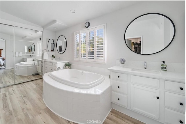 bathroom with a sink, a bath, wood finished floors, and two vanities