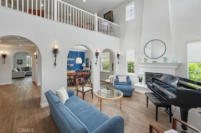living area with arched walkways, a high ceiling, baseboards, and wood finished floors