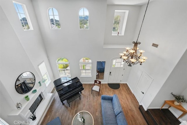 living area featuring visible vents, a towering ceiling, wood finished floors, baseboards, and a chandelier