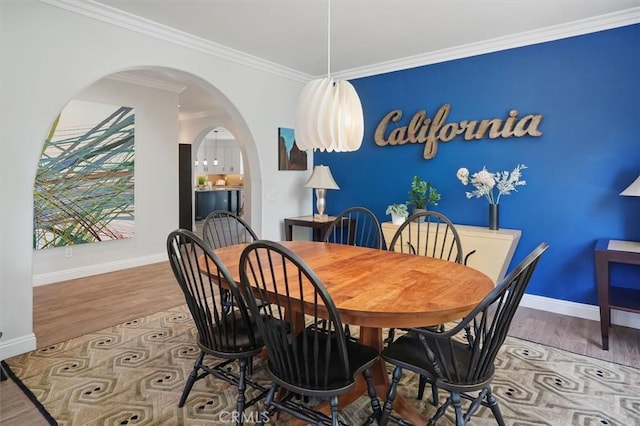 dining space featuring baseboards, arched walkways, wood finished floors, and ornamental molding
