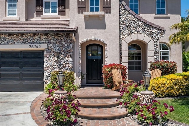 property entrance with concrete driveway, stucco siding, an attached garage, and stone siding