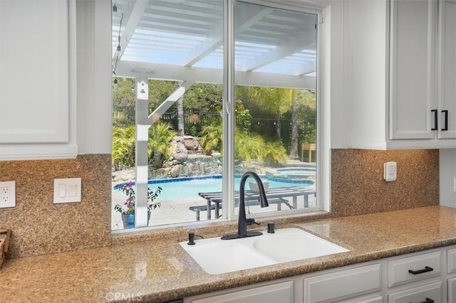 interior space with a sink, decorative backsplash, white cabinets, and a healthy amount of sunlight