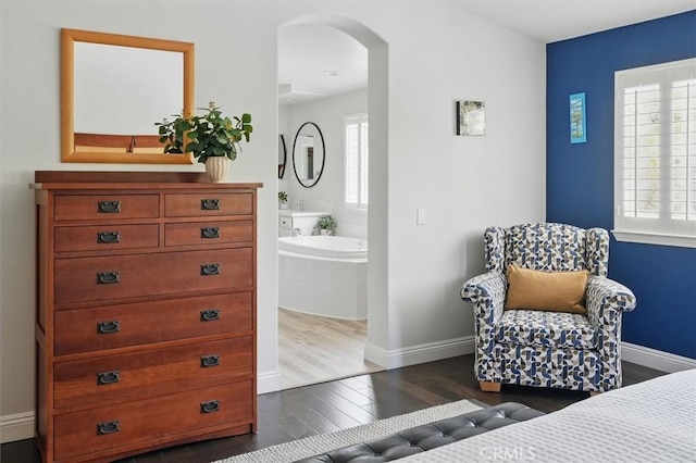 bedroom featuring dark wood-type flooring, arched walkways, baseboards, and multiple windows
