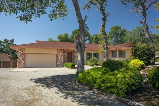 ranch-style house with a garage, gravel driveway, fence, and stone siding