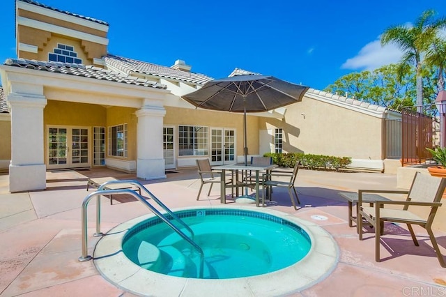 rear view of house with stucco siding, a community hot tub, a patio area, french doors, and a tiled roof