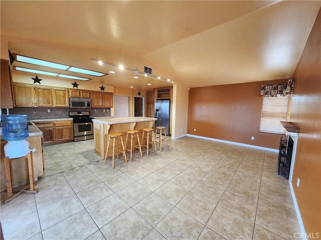 kitchen with tasteful backsplash, light tile patterned flooring, vaulted ceiling, a kitchen island, and appliances with stainless steel finishes
