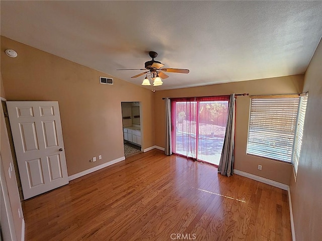 spare room with a ceiling fan, vaulted ceiling, baseboards, visible vents, and wood finished floors