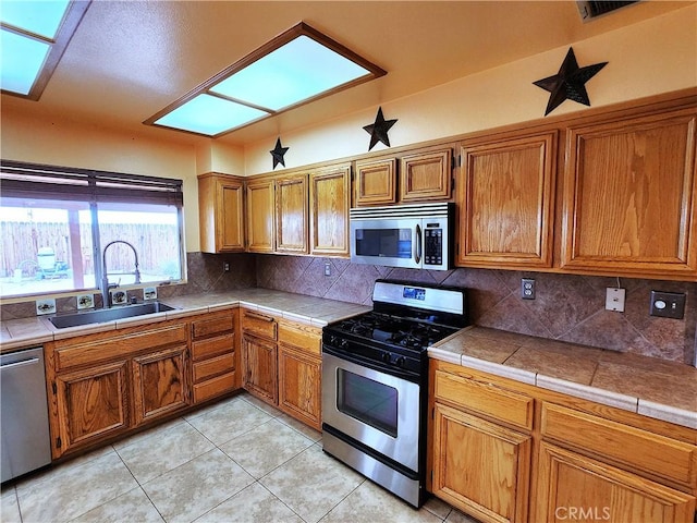 kitchen with a sink, brown cabinetry, appliances with stainless steel finishes, tasteful backsplash, and light tile patterned flooring