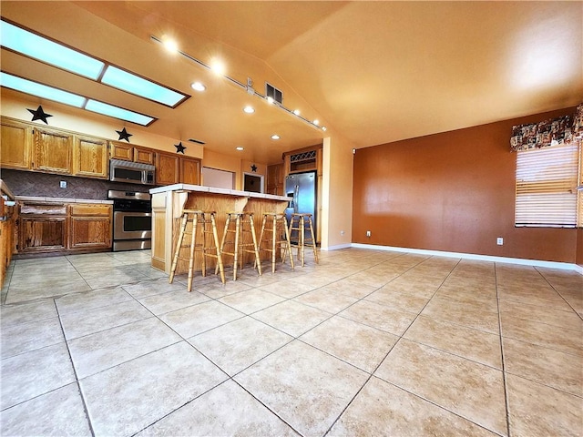 kitchen featuring brown cabinets, a breakfast bar, backsplash, light tile patterned floors, and appliances with stainless steel finishes