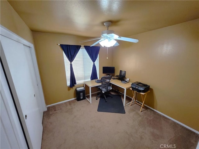 carpeted office space featuring baseboards and a ceiling fan