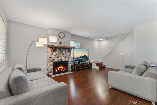 living room featuring dark wood-style flooring, visible vents, stairway, and a fireplace