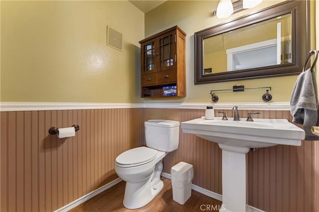 half bathroom with visible vents, wainscoting, wood finished floors, toilet, and a sink