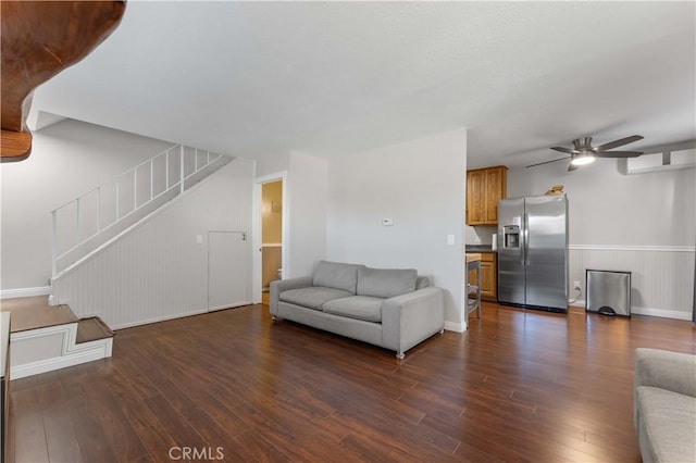 living room featuring a ceiling fan, stairs, a wainscoted wall, and dark wood-style floors