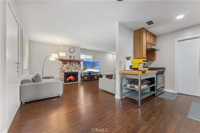 kitchen featuring a stone fireplace, visible vents, stainless steel range with gas stovetop, dark wood finished floors, and under cabinet range hood