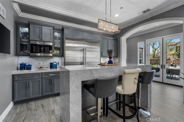 bar featuring crown molding, bar, arched walkways, visible vents, and stainless steel built in refrigerator