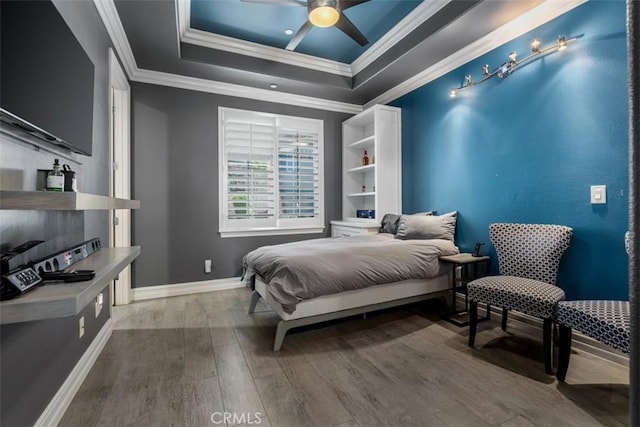 bedroom with ceiling fan, baseboards, wood finished floors, a tray ceiling, and ornamental molding