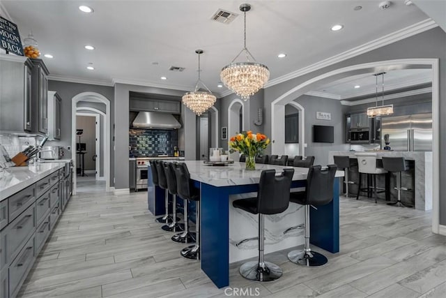 kitchen with gray cabinetry, arched walkways, backsplash, and under cabinet range hood