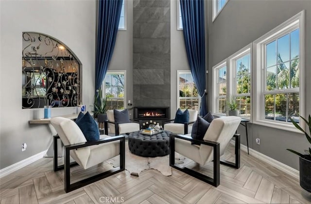 living area featuring baseboards, a high ceiling, a large fireplace, and a wealth of natural light