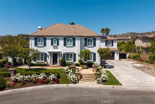colonial-style house featuring an attached garage, a tile roof, stucco siding, roof mounted solar panels, and driveway