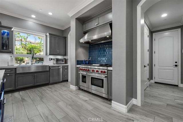 kitchen featuring ornamental molding, light countertops, under cabinet range hood, a sink, and appliances with stainless steel finishes