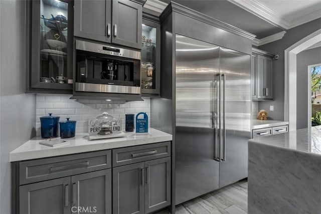 kitchen with ornamental molding, backsplash, built in fridge, and gray cabinetry