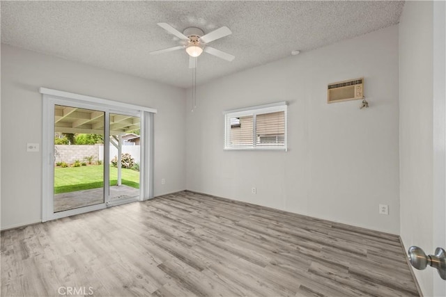 empty room with a wall mounted air conditioner, a textured ceiling, a ceiling fan, a wealth of natural light, and wood finished floors