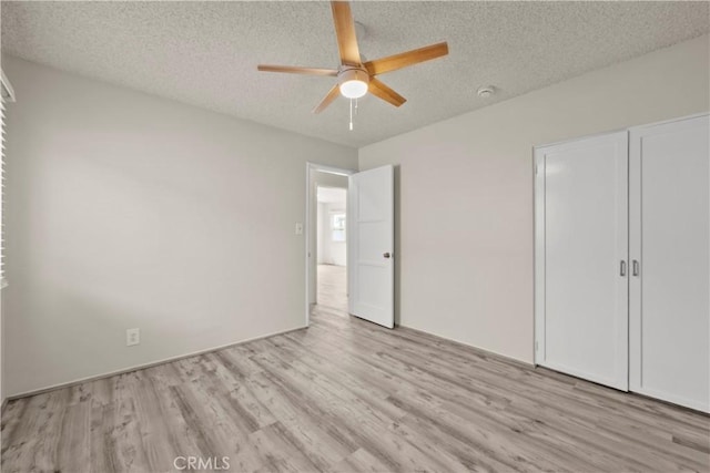 unfurnished bedroom with light wood-style floors, a textured ceiling, ceiling fan, and a closet