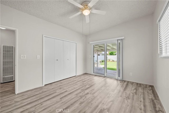 unfurnished bedroom with access to outside, a heating unit, light wood finished floors, and a textured ceiling