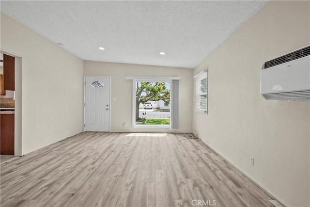 unfurnished living room featuring recessed lighting, a wall mounted AC, light wood finished floors, and a textured ceiling