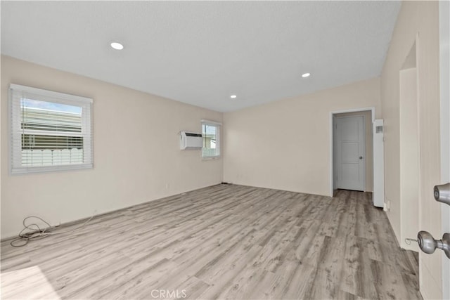 unfurnished room featuring recessed lighting, light wood-type flooring, and a wall mounted air conditioner