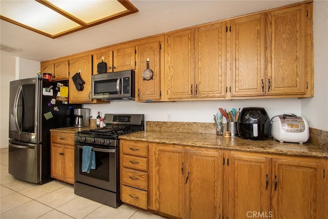 kitchen featuring light tile patterned floors, appliances with stainless steel finishes, brown cabinets, and visible vents