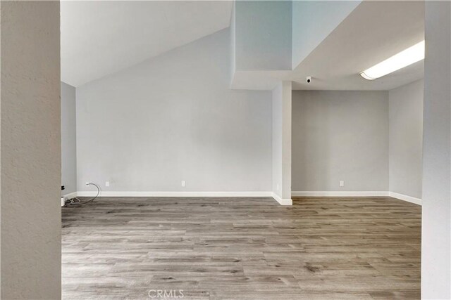 empty room with baseboards, lofted ceiling, and wood finished floors