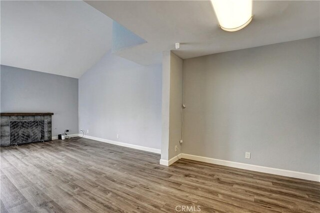unfurnished living room with baseboards, a fireplace, vaulted ceiling, and wood finished floors