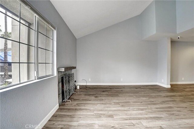 unfurnished living room with baseboards, high vaulted ceiling, wood finished floors, and a fireplace