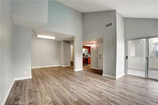 unfurnished living room with high vaulted ceiling, baseboards, wood finished floors, and visible vents