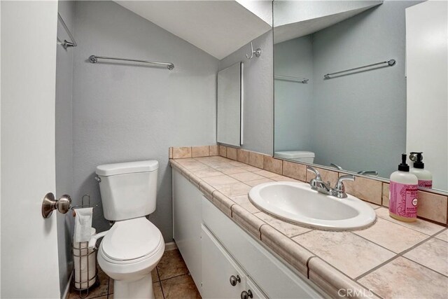 bathroom with toilet, tile patterned floors, lofted ceiling, and vanity