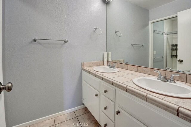 full bath featuring double vanity, a sink, a shower with shower door, and tile patterned floors