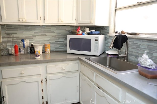 kitchen with white cabinets, backsplash, light countertops, and white microwave