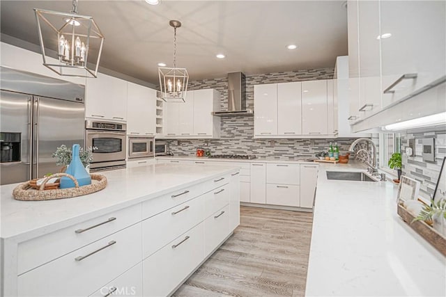 kitchen featuring appliances with stainless steel finishes, open shelves, white cabinetry, a sink, and wall chimney exhaust hood