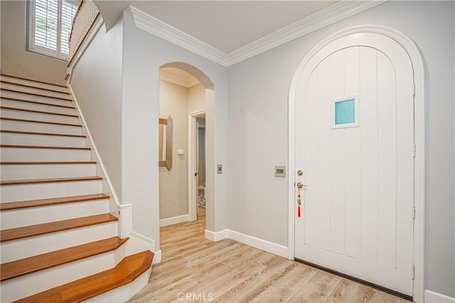 foyer entrance with stairs, arched walkways, crown molding, and light wood-type flooring