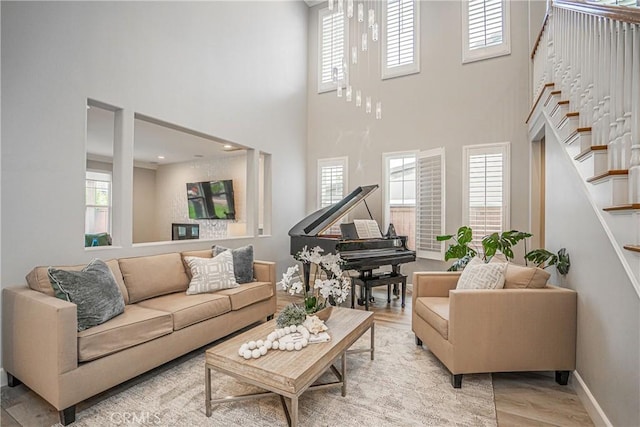 living room featuring baseboards, light wood-style flooring, stairway, and a towering ceiling