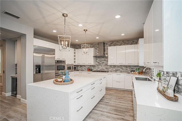 kitchen with visible vents, wall chimney range hood, light wood-type flooring, a sink, and stainless steel appliances