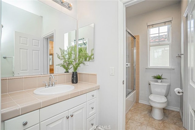 full bathroom featuring vanity, shower / bath combination with glass door, toilet, baseboards, and tile patterned floors