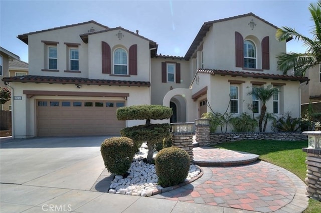 mediterranean / spanish-style home featuring a tiled roof, an attached garage, and stucco siding
