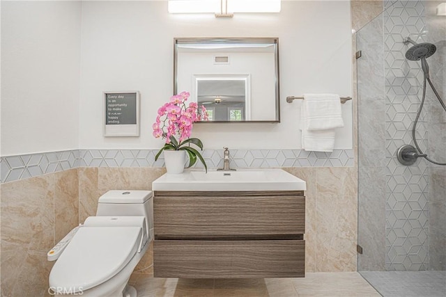bathroom with vanity, toilet, a wainscoted wall, tile walls, and tiled shower